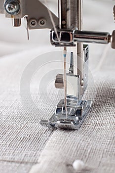 Modern sewing machine presser foot with linen fabric and thread, closeup