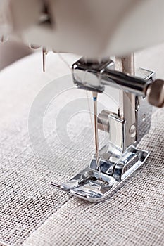 Modern sewing machine presser foot with linen fabric and thread, closeup