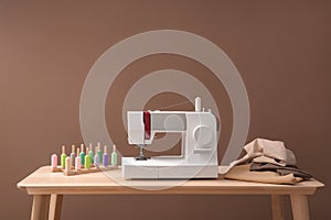 Modern sewing machine, set of threads and fabric on table against color background
