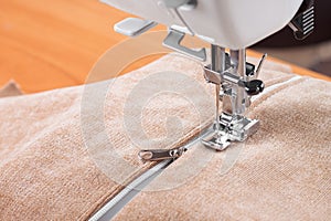Modern sewing machine special presser foot with beige fabric and zipper, closeup photo