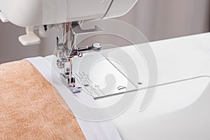 Modern sewing machine special presser foot with beige fabric and zipper, closeup photo