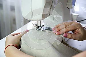 Modern sewing machine on a white table. A woman sews from linen fabric on a sewing machine