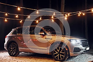 Modern silver colored automobile parked in forest with holiday decoration