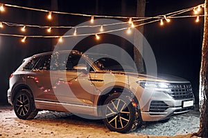 Modern silver colored automobile parked in forest with holiday decoration