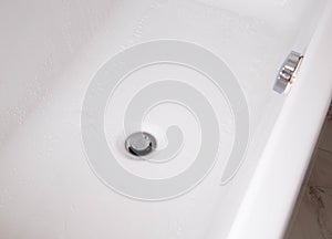 Modern silver drain plug in a new bathroom, water droplets on the walls of the bathtub. Copy space for text