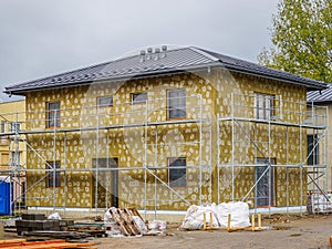 Modern single family two store home under construction, enclosed with scaffolds, thermal insulation