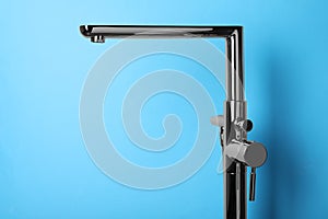 Modern single handle bathtub faucet on light blue background. Space for text