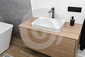 A modern sink in the bathroom with a matte black tap, the floor is covered with ceramic tiles imitating wood.