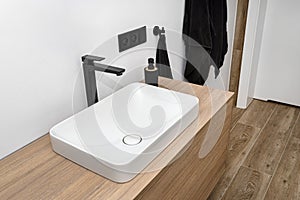 A modern sink in the bathroom with a matte black tap, the floor is covered with ceramic tiles imitating wood.