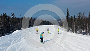 Modern ski resort in pine forest aeria, view from above. Footage. Young group of people snowboarding and skiing down the