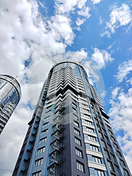 A modern skyscraper on the background of a blue sky with white clouds. View from below