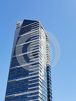 Modern skyscraper with glass facade and white stripes against blue sky, vertical