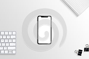 Modern smart phone with blank, white, isolated screen for mockup on flat, simple desk with keyboard, notepad and poster clips