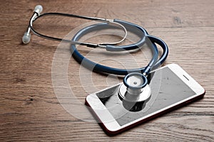 Modern smartphone with broken display and stethoscope on wooden table. Device repair service