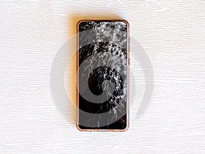 Modern smartphone with broken glass screen on white wooden background. Device needs repair