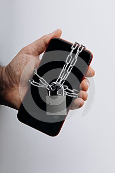 Modern smartphone with chain locked in man& x27;s hand. Social network issues and information security concept. Vertical