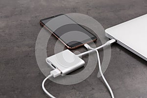 Modern smartphone and laptop charging from power bank on grey table, closeup