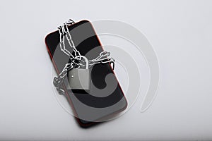 Modern smartphone locked by chain with padlock on a white table. Social network issues and information security concept