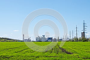 Modern soybean processing plant, agricultural Silos against green field and blue sky. Storage and drying of grains, wheat, corn,
