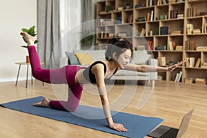 Modern sports, active lifestyle, training with online device. Slim asian lady in sportswear practicing yoga with laptop