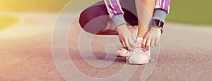 Modern sporty female runner tying shoelaces before going for a run in park