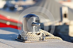 A modern stainless steel bollard with mooring on the dock in the harbor against the background of yachts on a sunny day. Outfittin