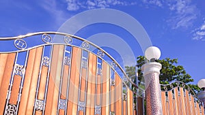 modern stainless steel and wooden sliding gate door with round lamp on mosaic pillar in front of home against blue sky