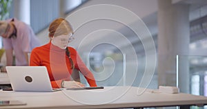 In a modern startup office, a professional businesswoman with orange hair sitting at her laptop, epitomizing innovation