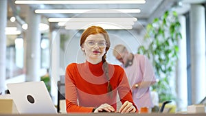 In a modern startup office, a professional businesswoman with orange hair sitting at her laptop, epitomizing innovation