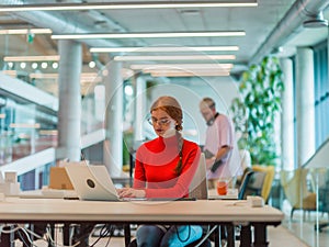 In a modern startup office, a professional businesswoman with orange hair sitting at her laptop, epitomizing innovation