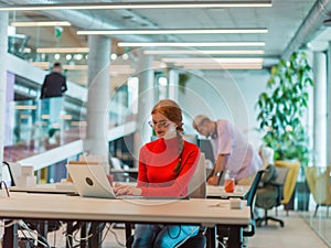 In a modern startup office, a professional businesswoman with orange hair sitting at her laptop, epitomizing innovation