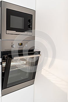 Modern steel microwave and opened oven in kitchen