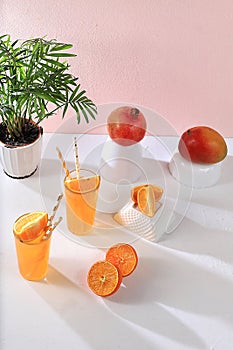 Modern still life with citrus, orange juice and oranges, pomegranate and mango on stand and podiums against pink background with