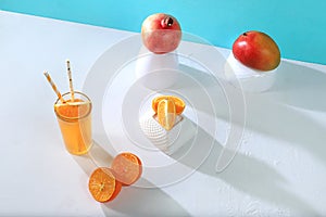 Modern still life with citrus, orange juice and oranges, pomegranate and mango on stand and podiums on blue background with long