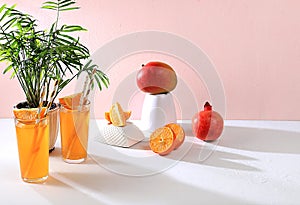 Modern still life with citrus, orange juice and oranges, pomegranate and mango on stand and podiums on pink background with long