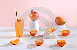 Modern still life with citrus, orange juice and oranges, pomegranate and mango on stand and podiums on pink background with long