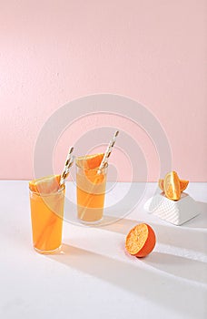 Modern still life with citrus, orange juice and oranges on stand and podiums against pink background with long hard shadows,