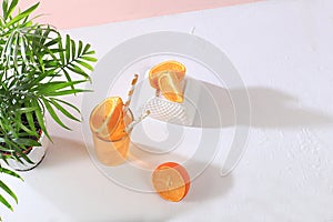 Modern still life with citrus, orange juice and oranges on stand and podiums against pink background with long hard shadows,