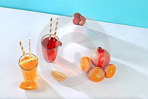 Modern still life with citrus, orange and strawberry juice and oranges, pomegranate and strawberries on stand and podiums on blue