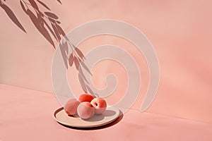 A modern still life featuring peaches on a beige plate, with a botanical shadow cast onto a textured pink wall.