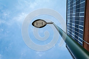 Modern street lamp, and the facade of a glass building, against a background of blue cloudy sky. Architectural background.