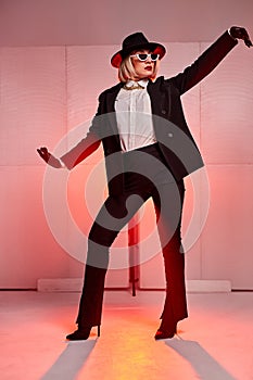 modern style dancer in suit and hat, sunglasses posing at camera, in studio on neon