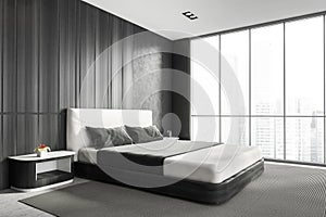 Modern stylish bedroom interior with wooden walls, concrete floor, master bed and panoramic window city view. Skyscraper building