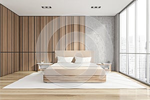 Modern stylish bedroom interior with wooden walls, parquet floor, master bed and panoramic window city view. Skyscraper building