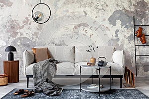 Modern and stylish living room with gray sofa with plaid, and rack with books and personal accessories. Gray concrete wall. Home