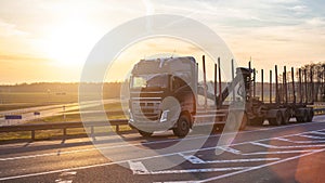 Modern stylish and reliable timber truck with a manipulator rides on the highway against the sunset, copy space