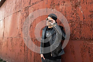 Modern stylish young hipster man in a leather stylish jacket in a fashionable black baseball cap in trendy dark sunglasses