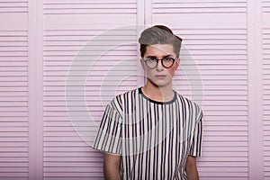 Modern stylish young man hipster in fashionable glasses with a hairstyle in a trendy striped t-shirt posing near a vintage wooden