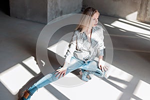 Modern stylish young sexy woman in a fashionable shirt in blue ripped jeans in green cowboy boots sitting in a sunny spring day