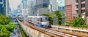 Modern subway electric train over ground on a bridge on stilts among skyscrapers metro with turn speed motion blur.